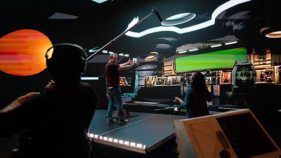 《菠菜台子大全》的导演杰森·墨菲站在一个虚拟宇宙飞船的舞台上. 他正在和一名工作人员交谈，另一名工作人员拿着吊杆麦克风.